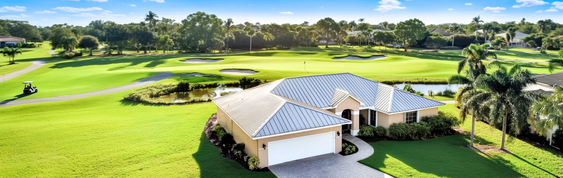 A single-story home with a metal roof next to a scenic golf course in Southwest Florida, surrounded by trees and lush landscaping.